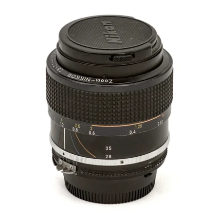 Objectif photo vintage Nikon Zoom-Nikkor 28-50mm f/3.5 AI-S posé debout avec son bouchon avant