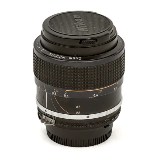 Objectif photo vintage Nikon Zoom-Nikkor 28-50mm f/3.5 AI-S posé debout avec son bouchon avant