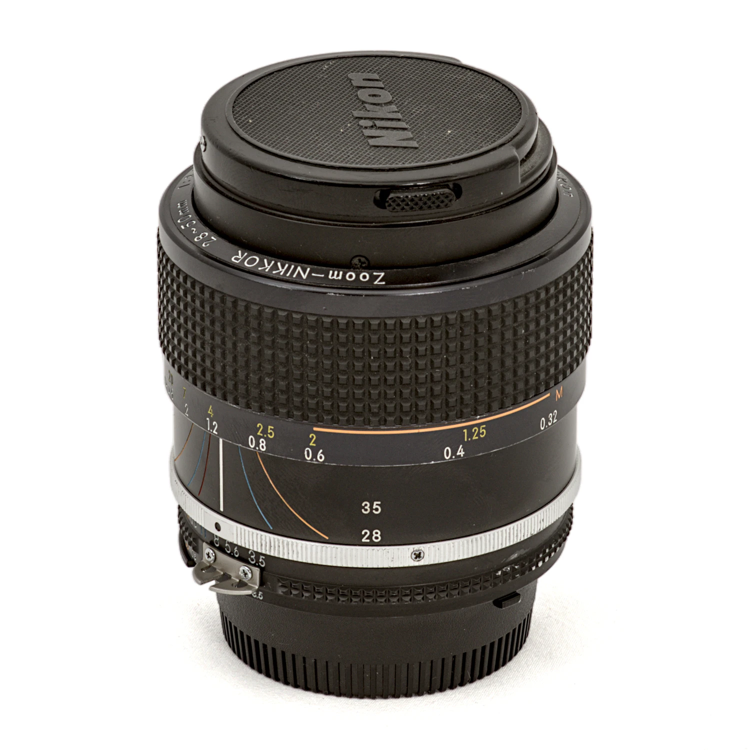 Objectif photo vintage Nikon Zoom-Nikkor 28-50mm f/3.5 AI-S posé debout avec son bouchon avant