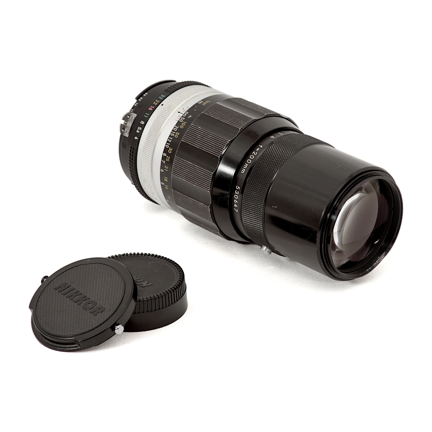 Objectif Nikon Nikkor 200mm f/4 couché montrant la lentille frontale et les bouchons