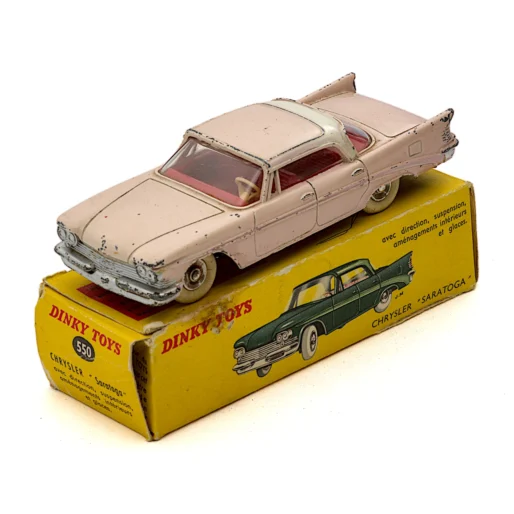 Miniature Dinky Toys 550 Chrysler Saratoga rose et blanche posée sur sa boîte d'origine jaune