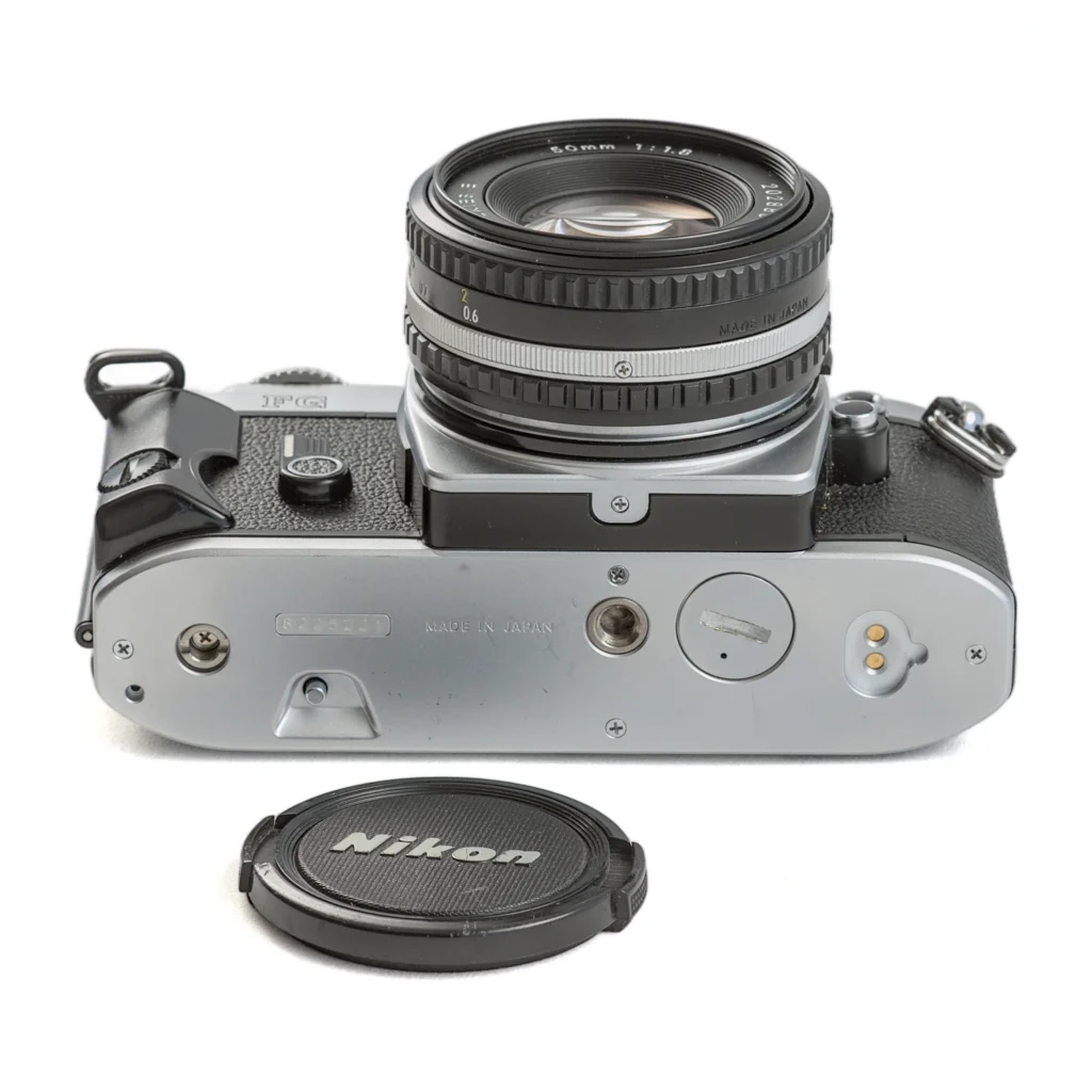 Vue de dessous de l'appareil photo Nikon FG avec le bouchon d'objectif posé à côté